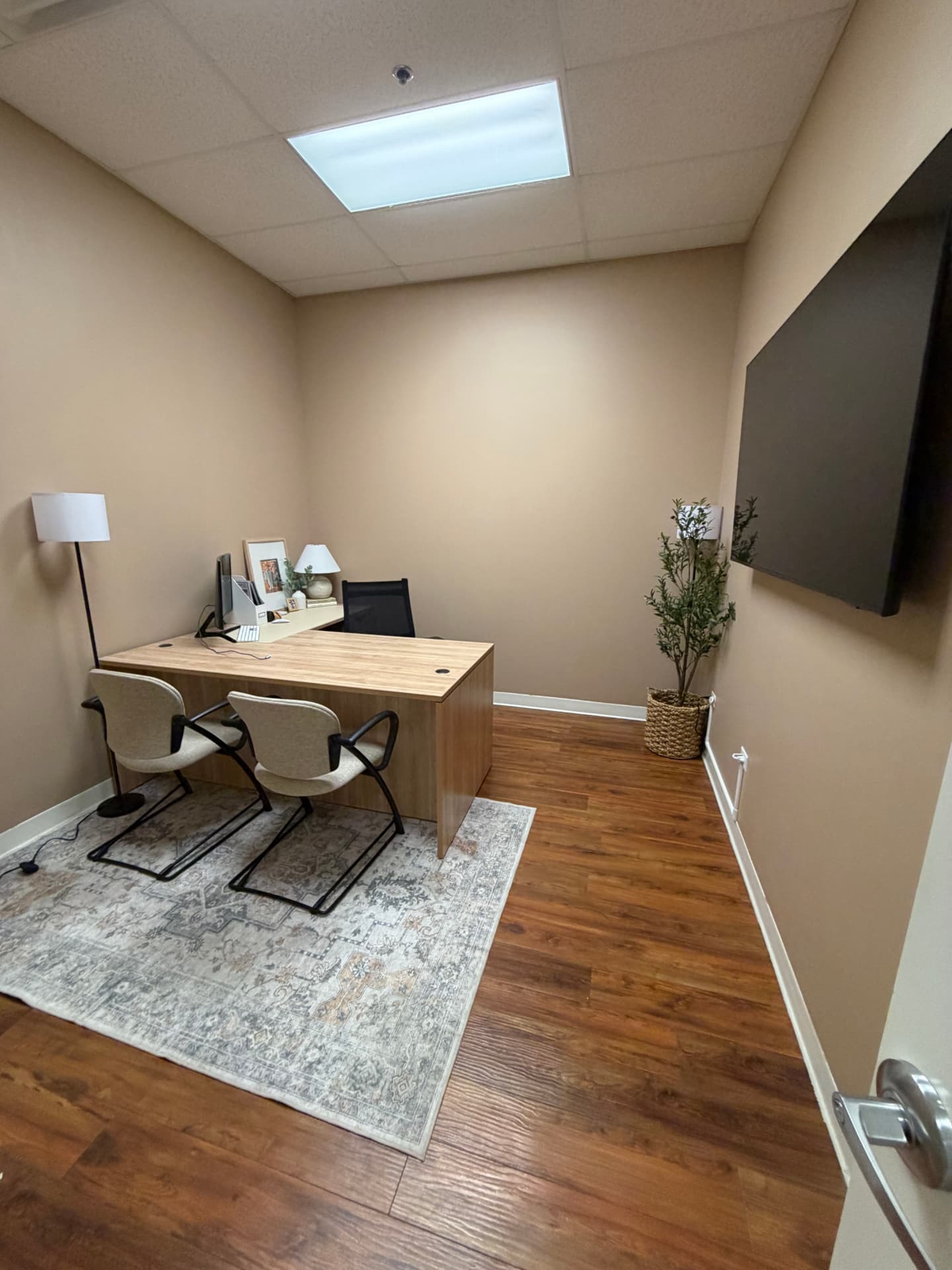 Large private suite with a desk, two guest chairs, floor lamp and a wall-mounted screen.